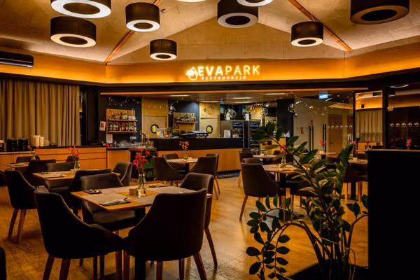 Sala restauracji wieczorem, ciepłe światło spod sufitu, czerwone goździki na stolikach